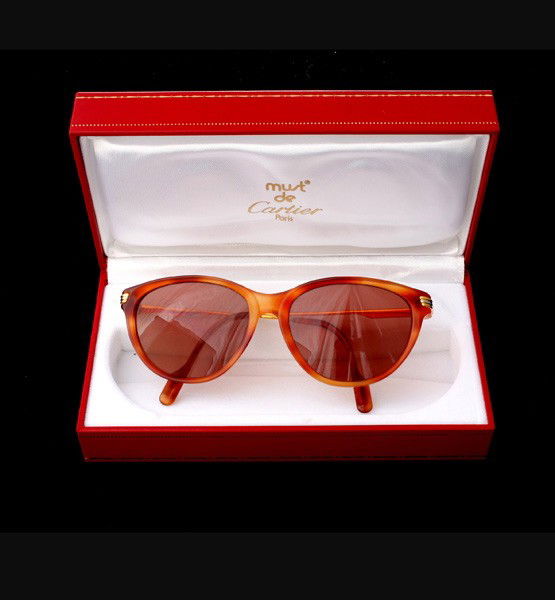 MUST DE CARTIER JASPE BLOND EYEWEAR.: MUST DE CARTIER JASPE BLOND EYEWEAR. The Must de Cartier sunglasses feature a light amber colored frame with gold tone accents, stamped Cartier. {Note: Includes original Cartier box and certificates;