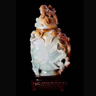 A Jadeite Carving of a Vase with Lid: A Jadeite Carving of a Vase with Lid, Of flattened baluster form emerging behind fruitful branches with roosting birds, the lid carved en suite, the icy green and white matrix with rusty red