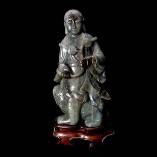 A Jade Carving of Liu Hai: A Jade Carving of Liu Hai, Executed from a substantial dark green stone of deep russet inclusions and veins throughout, depicting a robed figure, his shoulders draped with coins suspended by a rope,