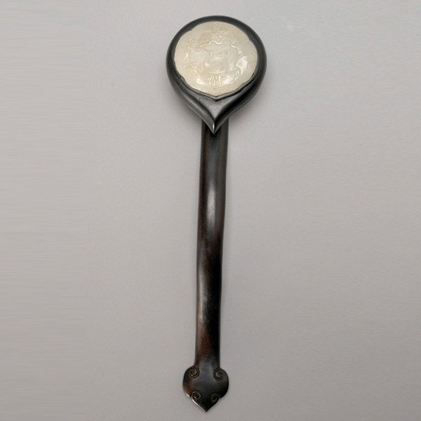 A Wood Ruyi Scepter Inset with a Jade Plaque: A Wood Ruyi Scepter Inset with a Jade Plaque, the jade carved with two cranes beneath a large pine tree {Length: 14 inches (35.6 cm)} [Cracks and wear to the wood, soiling to the jade]