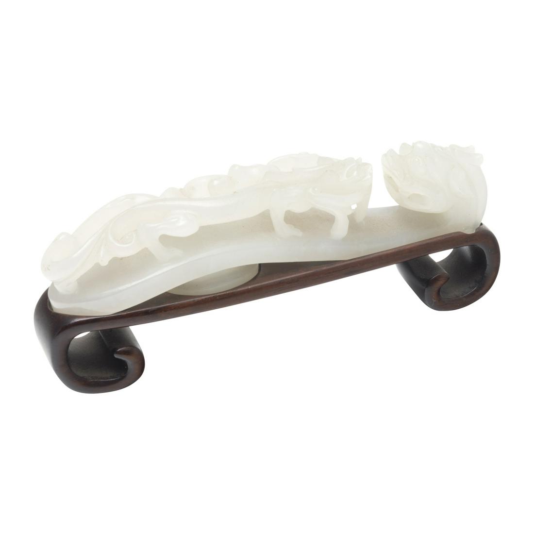 A Celadon Jade Reticulated Chilong Belt Buckle: A Celadon Jade Reticulated Chilong Belt Buckle on Stand. Carved in openwork from an even, pale stone with dragon head hook and confronting raised Chilong dragon holding a lotus sprig in its mouth, the