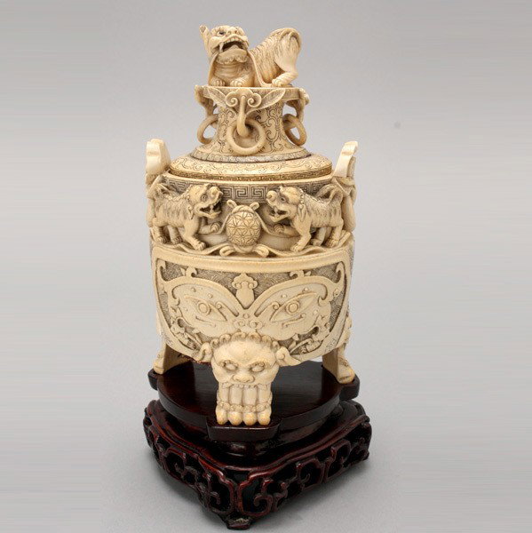 A Carved Ivory Censer*, Early 20th Century: A Carved Ivory Censer*, The globular body supported on three lion-head legs, the body carved with taotie masks, below four Fu dogs playing with two embroidered balls and a pair of ruyi-head handles wi