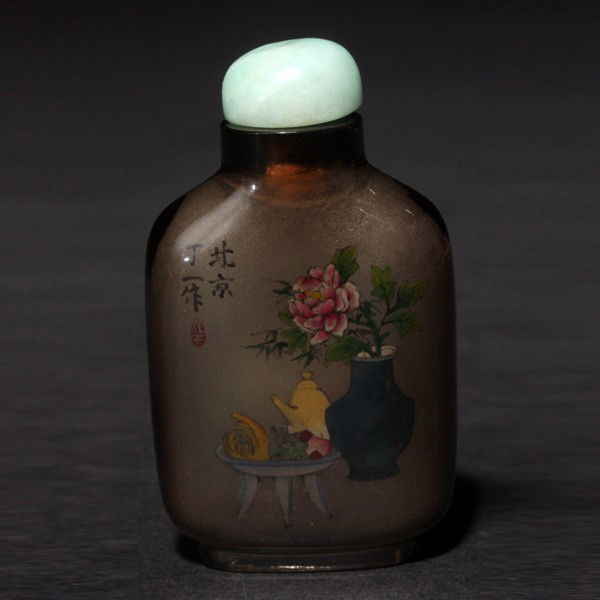 An Inside-Painted Crystal Snuff Bottle: An Inside-Painted Crystal Snuff Bottle, Depicting various antiquities, flowers and fruits, with jadeite stopper, the base bearing the signature and seal of 'Ding Yi'. Height: 2 3/8 inches (6 cm.)