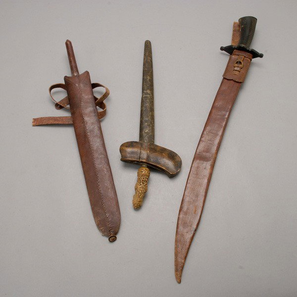 Three Large Knives in Sheaths: Kris with Metal Scabbard; a machete with leather case; and and a sword with leather case {Length of longest blade 24 inches)