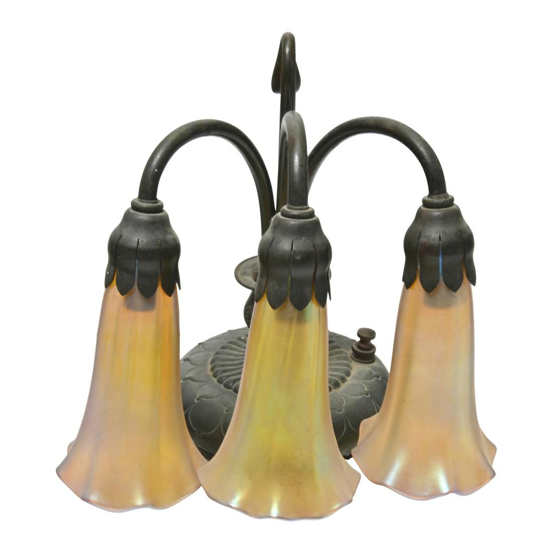 Tiffany Studios Three Light Bronze Piano Lamp.: Tiffany Studios Three Light Bronze Piano Lamp. The body in the form of a low vase, with the three lights emanating from the mouth, a sprig form hook behind the lights acts as a handle, switch to the b
