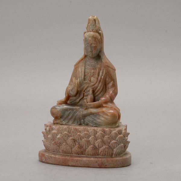 A Soapstone Guanyin: A Soapstone Guanyin, the calico-red colored stone carved to depict the bodhisattva dressed in a robe and seated in dhyanasana on a lotus platform, holding a bottle in her left hand {Height: 8 3/8 inch