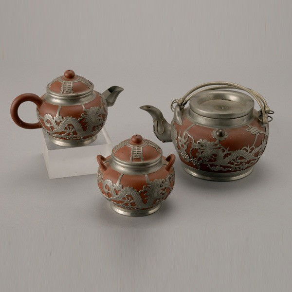 A Pewter Clad Yixing Tea Set, Republic Period: A Pewter Clad Yixing Tea Set, Republic Period, including a teapot, and covered creamer and sugar, each decorated with dragons and 'shou' characters, a stamped mark to each base {Tallest Teapot: 4 1/2