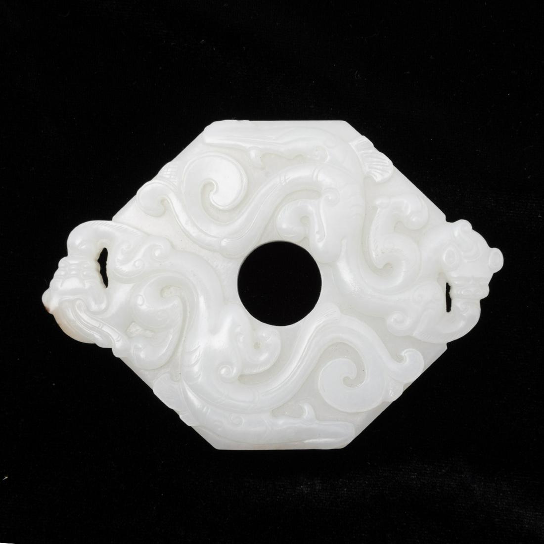 A Chinese Carved Jade Archaistic Dragon Pendant: A Chinese Carved Jade Archaistic Dragon Pendant. Of hexigonal form, carved to each side with archaistic dragons, the stone is of light celadon hue. {Width 4 1/8 inches (10.4 cm)}.