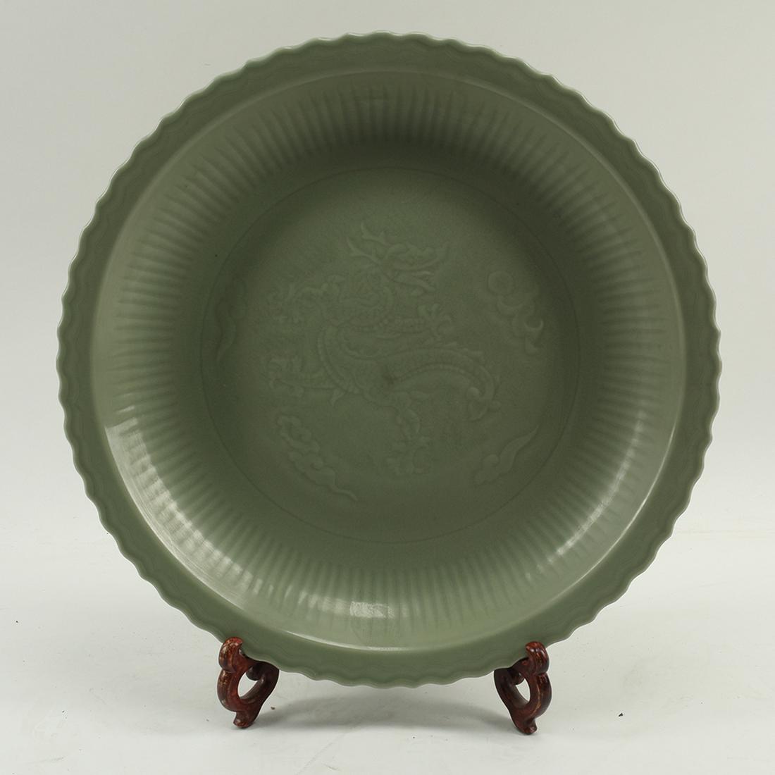 A Massive Chinese Longquan Celadon Porcelain Charger: A Massive Chinese Longquan Celadon Porcelain Barbed-Rim Charger. The dish is heavily potted with fluted sides rising from the low foot ring to the everted, barbed rim. the center well carved with drag