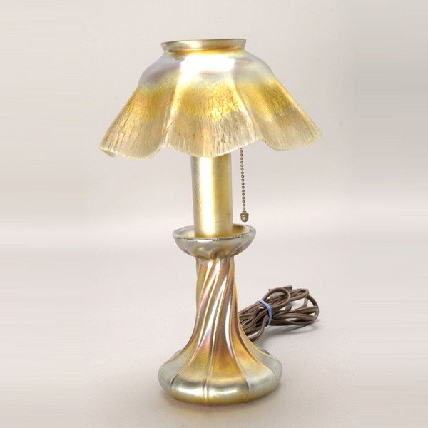 Tiffany Studios gold favrile candlelamp: Tiffany Studios Gold Favrile Candlelamp. The twisted candlestick base fitted with a ruffled rim shade veined with stretch iridescence of gold, blue and violet highlights on its ground, internally deco