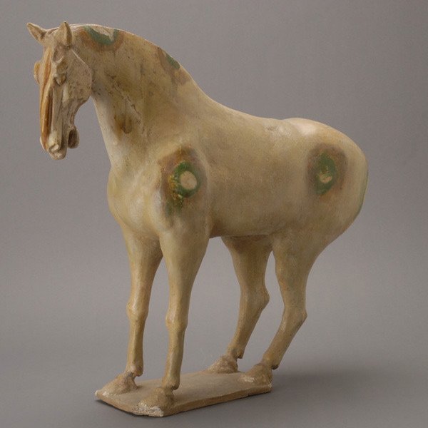 A Tang Straw-Glazed Pottery Horse, Tang: A Tang Straw-Glazed Pottery Horse, Standing foursquare on a rectangular base, with head turned slightly to the side and mouth open, covered in a streaked straw and ochre-colored glaze. Tang Dynasty He