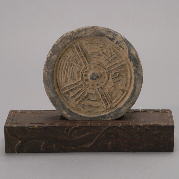 A 'Wadang' (Roof End): A 'Wadang' (Roof End), of circular form carved with 'Chang Le Weiyang' (Infinite Joy), with a matching wood stand with dragon and key fret design {Diameter: 6 1/2 inches (16.5 cm)} [Wear, losses]