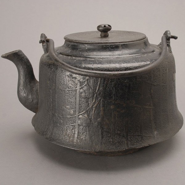 A Japanese Cast Iron Kettle: A Japanese Cast Iron Kettle, subtly decorated with prunus branches {Height: 7 3/4 inches (19.5 cm) not including handle} [Minor losses and holes to the finial]
