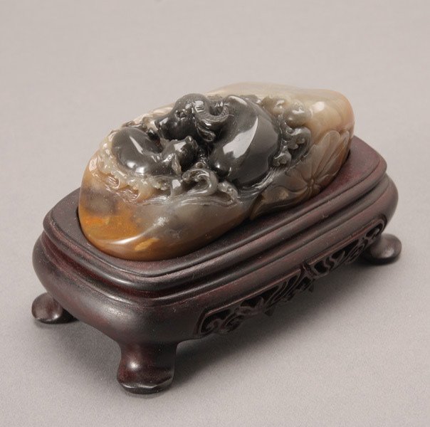 A Soapstone Carving of Water Buffalos: A Soapstone Carving of Water Buffalos, depicting the two beasts amidst curling waves above a large lotus leaf, with wood stand {Length of Carving: 4 inches (10.2 cm)}