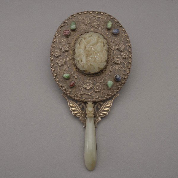 A Silver-Mounted Mirror with Jade Handle, 19th C: A Silver-Mounted Mirror with Carved Jade Handle, With a celadon jade dragon belt-hook forming the handle, the mirror back mounted with a pale celadon oval plaque carved with a chilong dragon, all enci