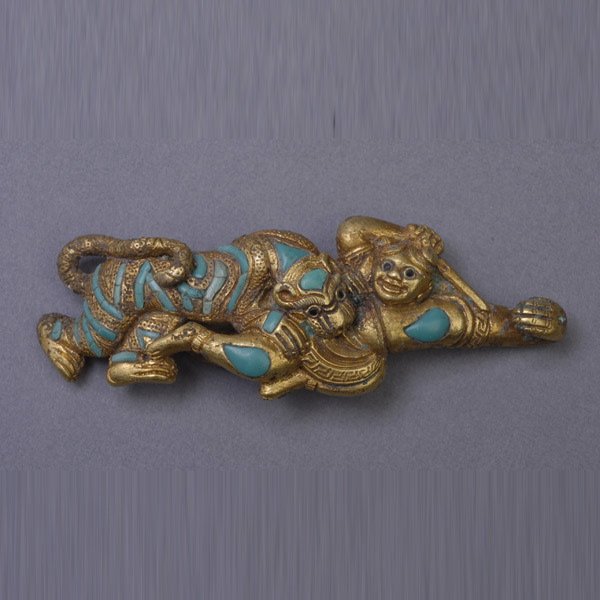 A Gilt-Bronze Bell Hook, Possibly Yuan Dynasty: A Gilt-Bronze Bell Hook, Cast as a figural group depicting a warrior slaying a tiger with a sword, the tiger's strips and the warrior highlighted with turquoise inlay. Possibly Yuan Dynasty, Length: 2