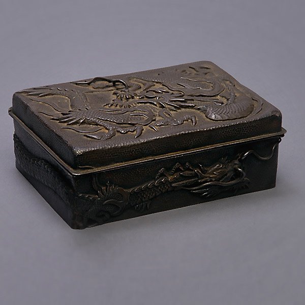 A Repousse Silver 'Dragon' Box: A Repousse Silver 'Dragon' Box, of rectangular form with a hinged lid, decorated with two large dragons to the lid and sides {Width: 5 inches (12.7 cm)} [Tarnish, missing one whisker, dents, abrasions