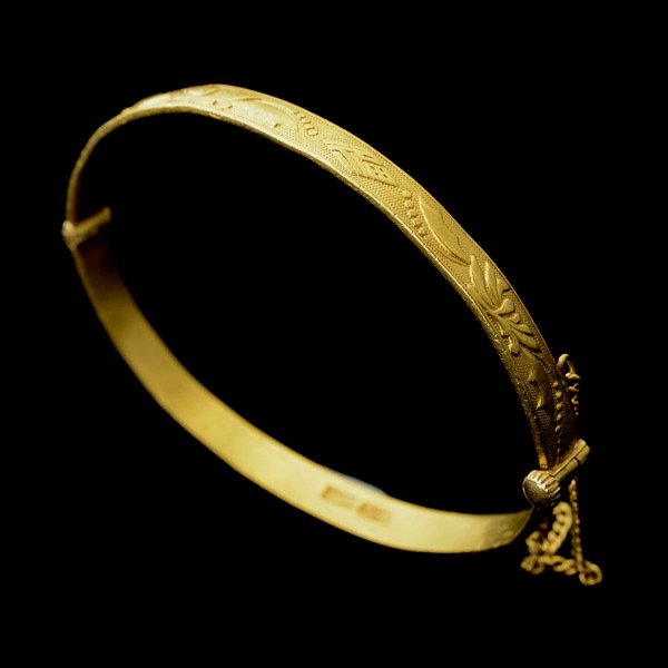 22K YELLOW GOLD BRACELET.: 22K YELLOW GOLD BRACELET. The hinged 22k yellow gold bangle measuring approximately 5.00 mm with a total largest internal diameter of 55 mm, exhibits a foliate and geometric motif in relief, completed