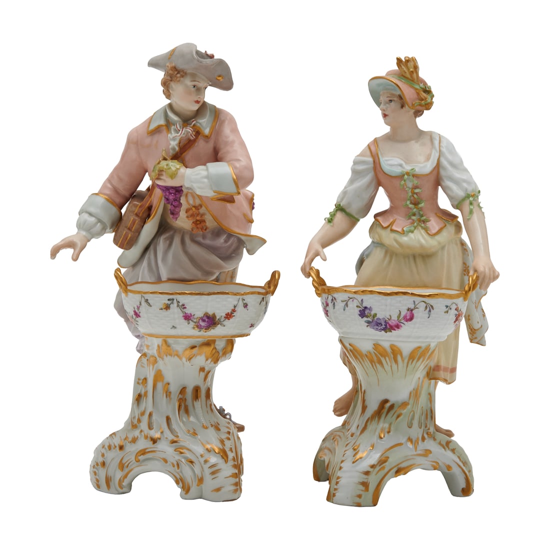 Two KPM Porcelain Figural Salts: Two KPM Porcelain Figural Salts, formed as rustic farmers in 18th Century dress, each with a large two handeled basket painted with flowers before them, on tripodal scroll bases picked out in gidling.