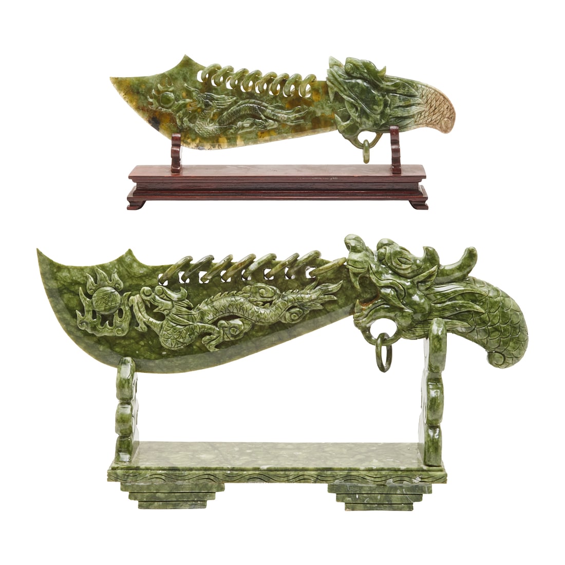 Two Chinese Carved Jade Dragon Swords on Bases: Two Chinese carved jade swords, each with a sweeping curved blade and a raised display base. The blades are worked with sinuous dragons in relief along the edges and terminals, the mouths open grippin