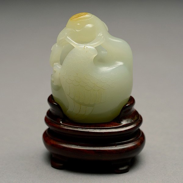 A Small Jade Goose Carving: A Small Jade Goose Carving, of rounded form shown holding a lingzhi branch with a light russet inclusion, wood stand {Height: 1 3/4 inches (4.4 cm)}