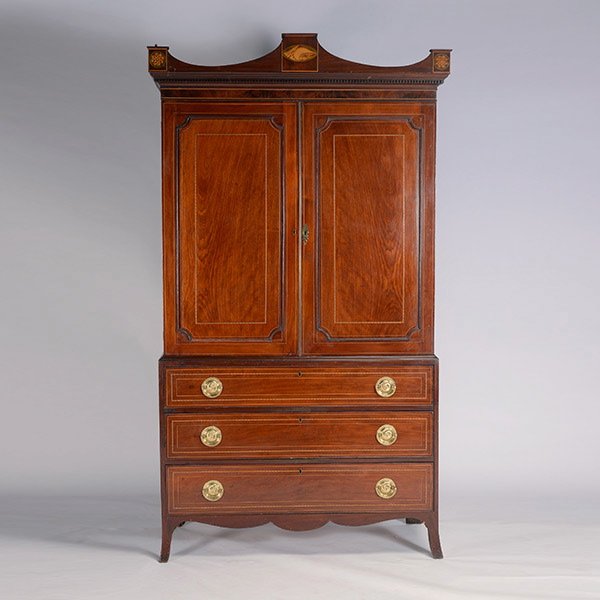 George III Style Mahogany Linen Press: George III Style Mahogany Linen Press. The outswept scalloped pediment top centering an inlaid shell adorsed by rosette corner mounts, over twin paneled doors enclosing a shelved interior, over three 