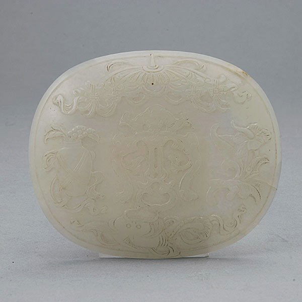 A White Jade Plaque: A White Jade Plaque, the domed ovoid form carved in relief with a bat chime above a fish, flanked by flowers and a vase, all beneath a tasseled parasol {Width: 4 inches (10.2 cm)} [Small chips to the