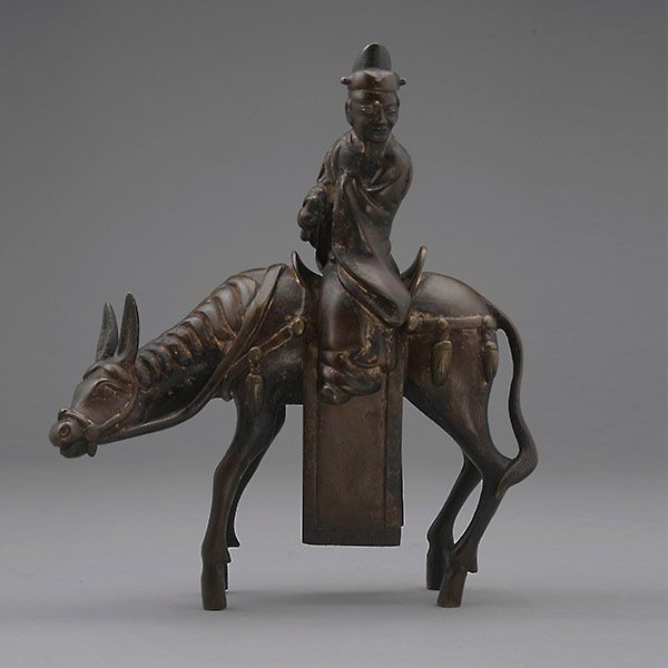A Bronze Figural Censer, Qing Dynasty: A Bronze Figural Censer, Depicting Su Shi, the Song Dynasty official and calligrapher, holding a scroll of calligraphy as he rides upon a mule. Qing Dynasty, Height: 8 3/4 (22.2 cm) Provenance:Mr. and