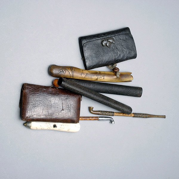 2 Japanese Leather Tobacco Pouches & Four Pipes: Two Japanese Leather Tobacco Pouches, fitted with a pipe and either a bone or woven pipe case; a third bamboo stemmed pipe; and a carved bone pipe bowl with carved monkeys (4) {Length of bamboo pipe 8