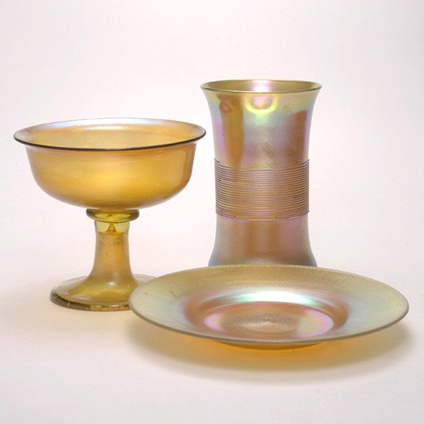 Three Tiffany Favrile Glass Items.: Three Tiffany Studios Favrile Glass Pieces. Comprising a gold semi-translucent footed sherbet cup; a tumbler with threaded banding; an undertray: the tumbler engraved "LCT T3149"; the sherbet "LCT Fav