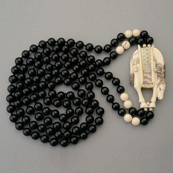 BLACK ONYX NETSUKE NECKLACE.: BLACK ONYX NETSUKE NECKLACE. Featuring a carved and painted netsuke depicting a horse, suspended from a double strand black onyx bead necklace measuring approximately 34 inches in length.