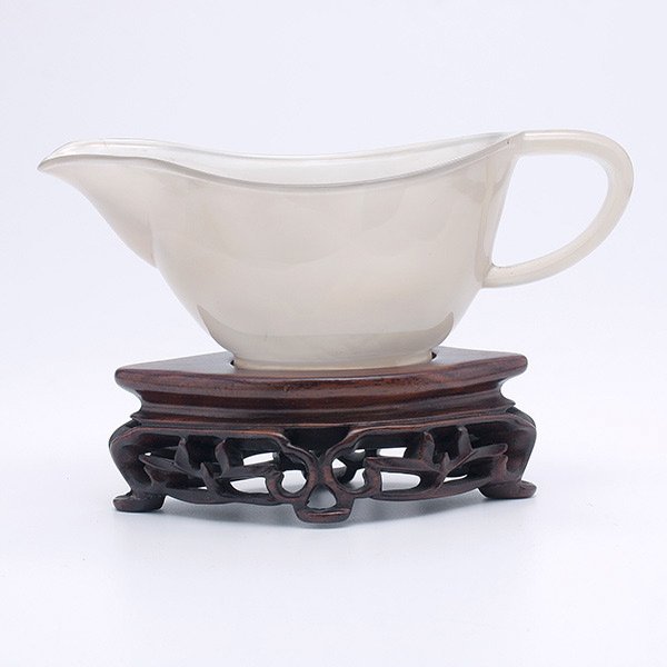 An Agate Wine Vessel: An Agate Wine Vessel, The elongated pouring vessel carved with an arching handle and a wide mouth, matching reticulated wood stand. Length: 5 1/4 inches (13.3 cm) [Small chip.This condition report sta