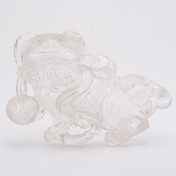 A Rock Crystal Model of a Buddhist Lion, 20th C.: A Rock Crystal Model of a Buddhist Lion, The Buddhist symbol shown seated and grasping a ribbon with a brocade ball attached. 20th Century, Length: 6 inches (15.3 cm)