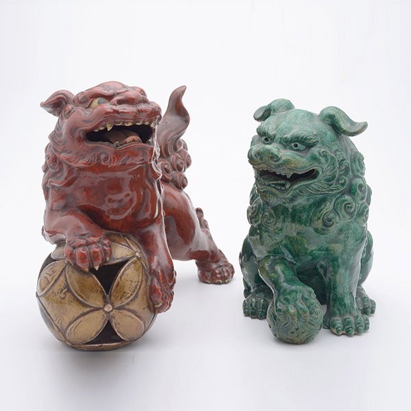 Two Glazed Ceramic Buddhist Lions: Two Glazed Ceramic Buddhist Lions, one red-glazed and one green-glazed, both depicted with open mouths while accompanied by patterned spheres, marks to each {Taller: 9 inches (23 cm)} [Repairs, wear, 