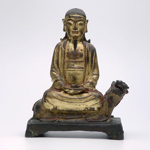 An Unusual Bronze Model of Guanyin, Early Ming Dynasty: An Unusual Cast Bronze Model of Guanyin Modeled wearing long robes and sitting on the back of a recumbent Buddhist lion, both hands holding a bowl in his lap, all on a footed platform. Early Ming Dyna