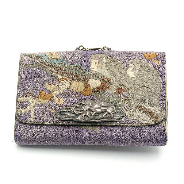 A Japanese Embroidered Tobacco Pouch: A Japanese Embroidered Tobacco Pouch Decorated with monkeys sitting in a leafy tree against a purple ground, with decorative white metal mounts and closure, a figural netsuke suspended by multiple cha