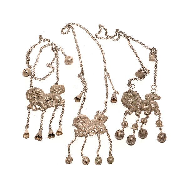 Three Silvered Lion Necklaces: Three Silvered Lion Necklaces Each necklace suspending a small lion-form pendant, two with moveable features, the various simplistic chains further suspending tassel ornaments with shaped metal bells.