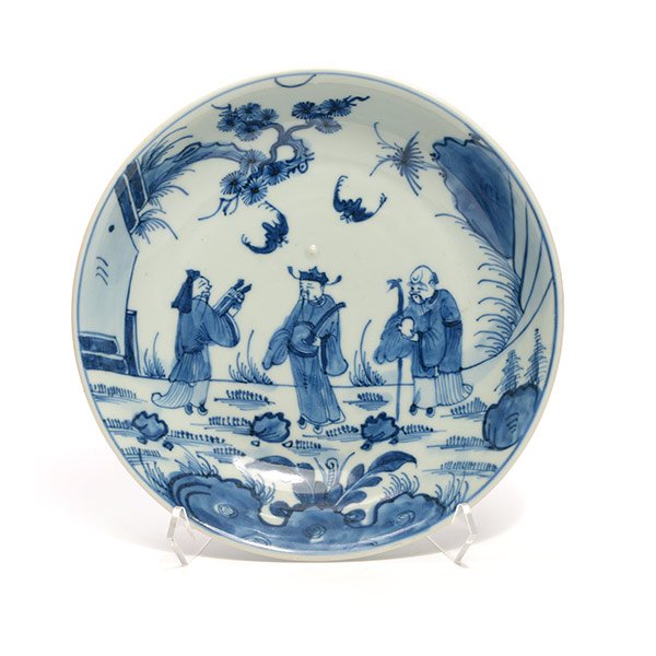 An Underglaze Blue Saucer: An Underglaze Blue Saucer The export saucer decorated with figural landscapes in blue and white, a stylized floral mark to the base. {Width: 7 3/4 inches (20 cm)} [Chips, minor abrasions]