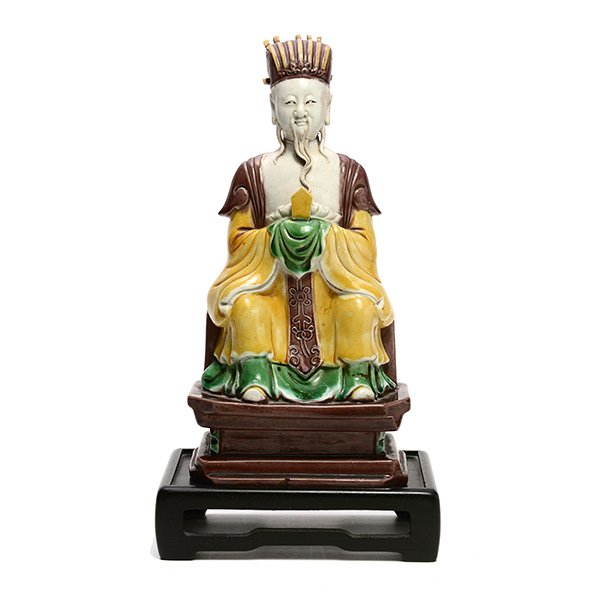 A Glazed Porcelain Daoist Immortal, Ming Dynasty: A Glazed Porcelain Daoist Immortal Covered in yellow, green and aubergine glazes, the immortal is shown seated holding a tablet that rests on his cloth-draped hands, wearing a ribbed court hat secured