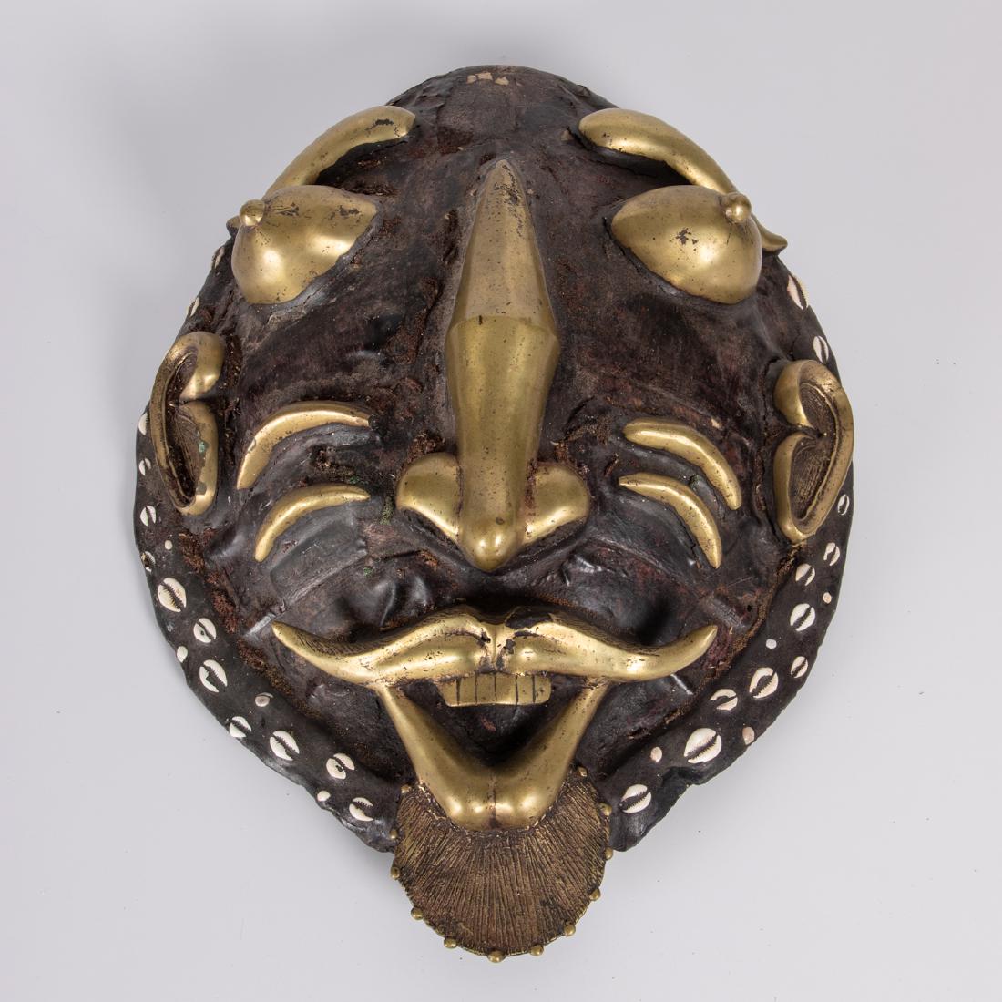 A West African Turtle Shell, Gilt Metal and Cowrie: A West African Turtle Shell, Gilt Metal and Cowrie Shell Hanging Figural Mask, 20th Century. H: 24 1/2 in. The Estate of Ronald J. DiCenzo, Professor of Japanese History, Oberlin College (1972-2005).