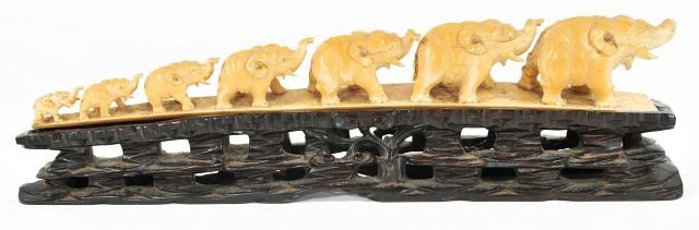 A Carved Ivory Tusk in the Form of Seven Marching E: A Carved Ivory Tusk in the Form of Seven Marching Elephants, Early 20th Century. On a carved wooden base. HEIGHT: 2 WIDTH: 13
