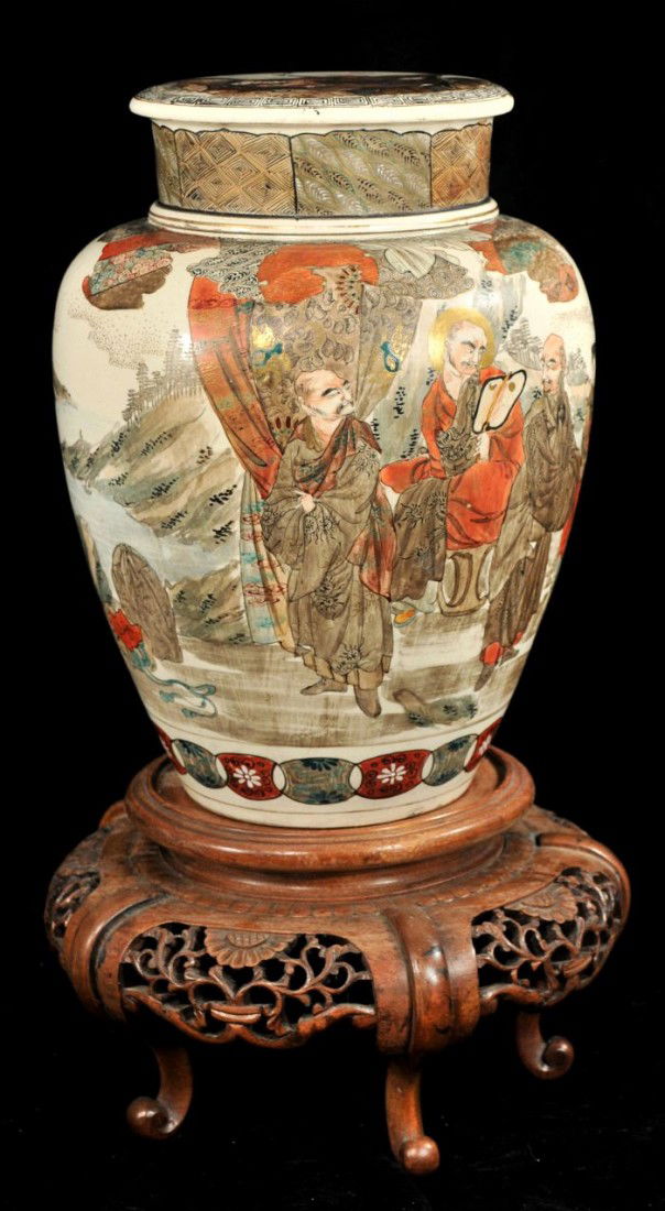 A Japanese Satsuma Earthenware Covered Vase, 19th: A Japanese Satsuma Earthenware Covered Vase, 19th Century, Depicting figures in a mountainous landscape, on a carved hardwood base and signed by the artist. h: 12 x w: 9 in.