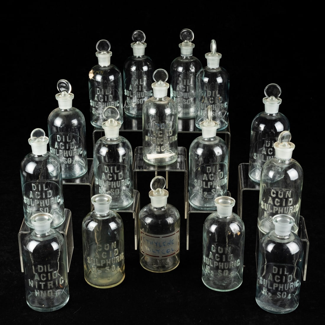 Glass Apothecary Bottles: Glass Apothecary Bottles, 20th Century. With fitted glass stoppers, raised and etched letters describing previous contents. Sixteen total, various sizes. Smallest: 6 1/2 in. high x 2 1/2 in. diameter 