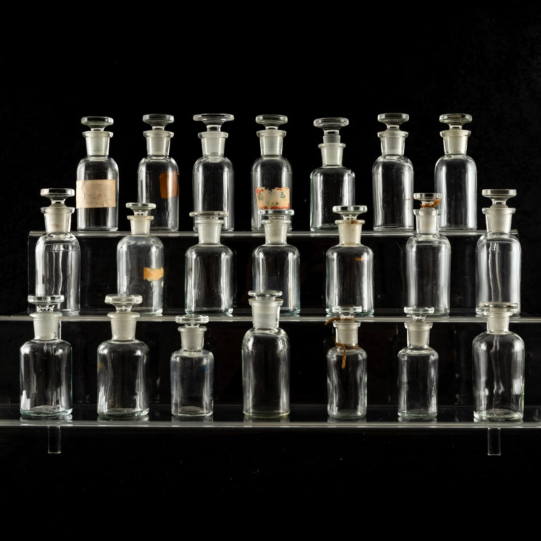 Glass and Radium Glass Apothecary Bottles: Glass and Radium Glass Apothecary Bottles, 20th Century. All with fitted glass stoppers, twenty one total, various sizes. Smallest: 3 1/4 in high x 1 1/4 in. diameter Largest: 4 3/8 in high x 1 1/2 in