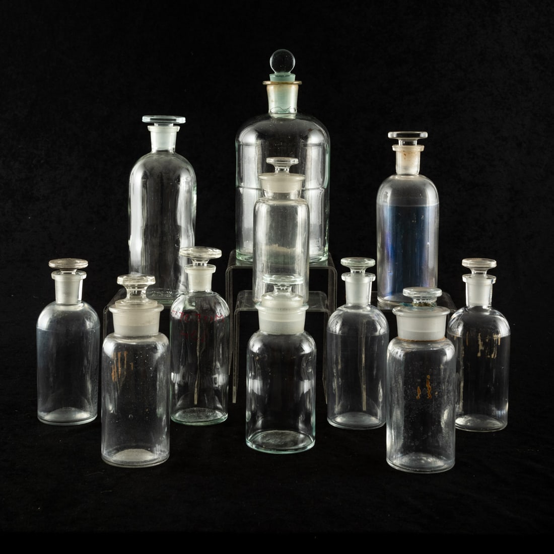 Glass and Radium Glass Apothecary Bottles: Glass and Radium Glass Apothecary Bottles, with fitted glass stoppers, 20th Century. Eleven total, various sizes. Smallest: 6 in. high x 2 3/8 in. diameter Largest: 9 3/4 in. high x 4 1/4 in. diameter