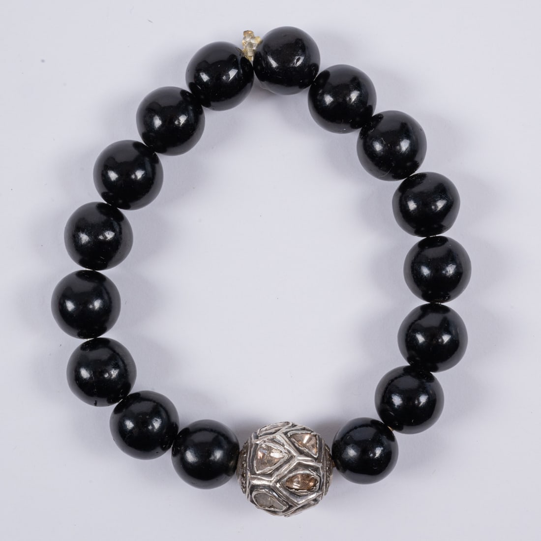 Beaded Wood And Diamond Bracelet: A Beaded Wood And Diamond Bracelet, With black wood beads, accented with a pave diamond melee bead composed of numerous flat cut diamonds set in silver. Strung on stretchy elastic cord. Metal tests as
