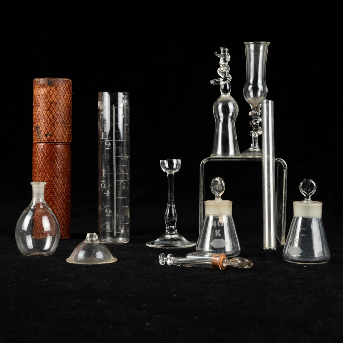 10 Diminutive Glass Laboratory Vessels: Ten Diminutive Glass Laboratory Vessels, 19th Century, Two Venetian blown glass doctor's vessels on pedestals entwined with a snake, a portable engraved apothecary's measure in a leather case, two