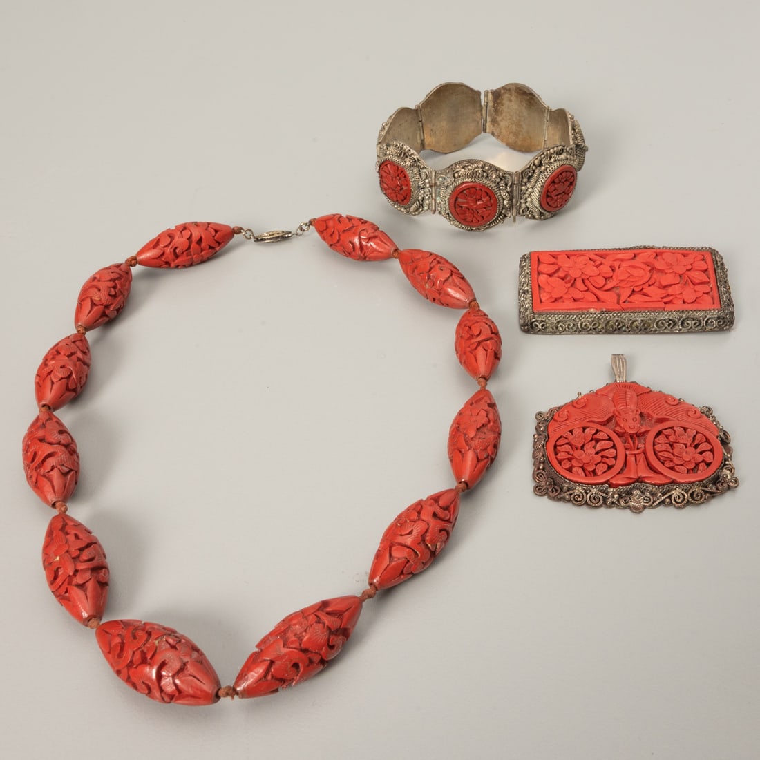 Four Chinese Silver and Cinnabar Jewelry Pieces: Four Chinese Silver and Cinnabar Jewelry Pieces, Comprising: A 17 inch beaded cinnabar necklace, bracelet, brooch and bat form pendant. Pendant size: 2 in x 2 in.