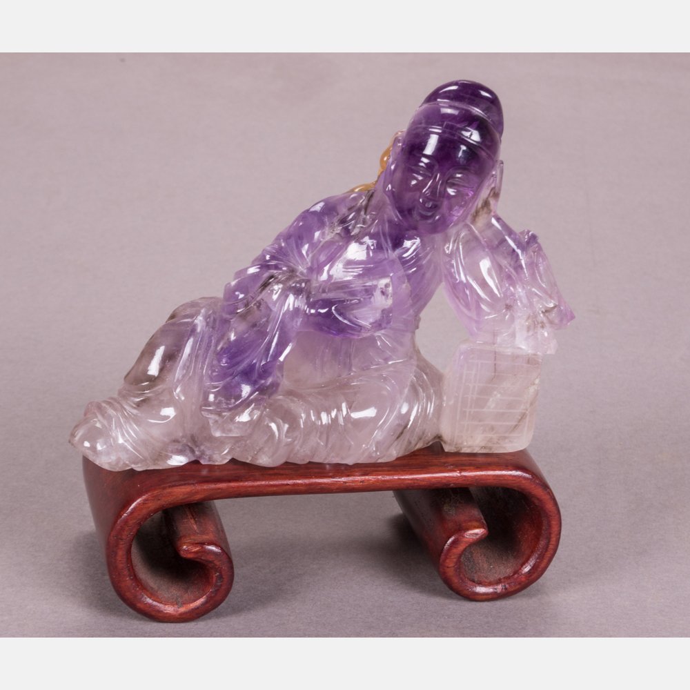 A Chinese Carved Amethyst of a Reclining Figure on a: A Chinese Carved Amethyst of a Reclining Figure on a Carved Hardwood Stand. H: 2 3/4 W: 3 3/4 D: 2 1/8 in.