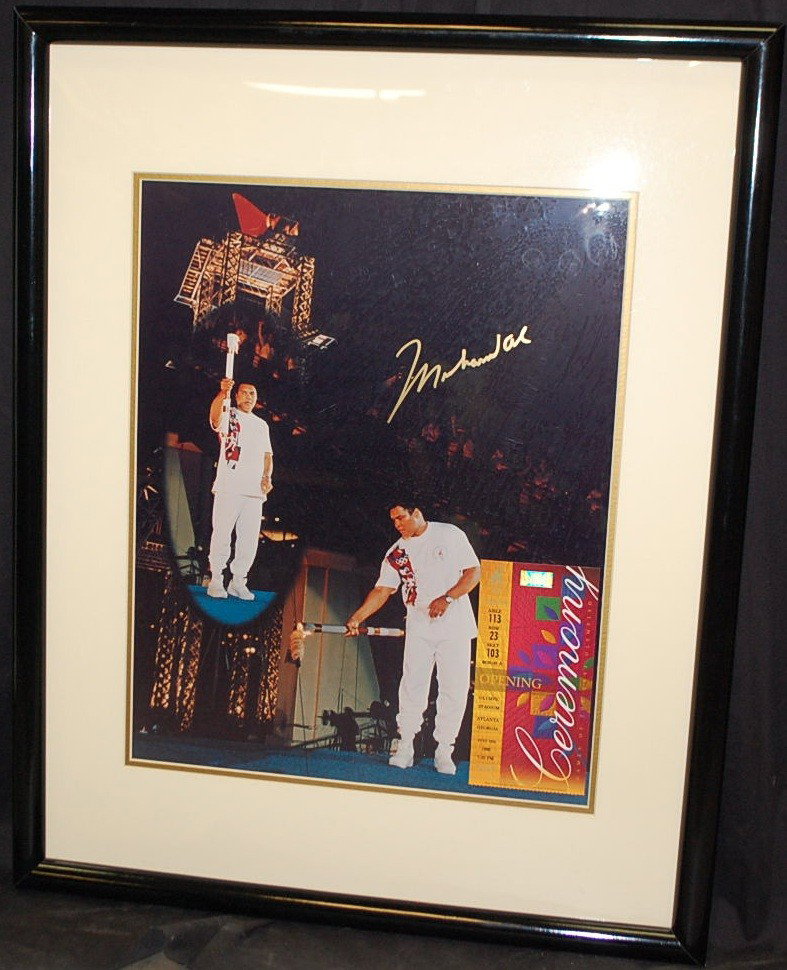 MOHAMID ALI AUTOGRAPH WITH OLYMPIC TORCH: FRAMED WITH OPENING TICKET TO THE 1996 OLYMPIC GAMES IN ATLANTA WITH COA AND PHOTO OF ALI SIGNING THE PICTURE